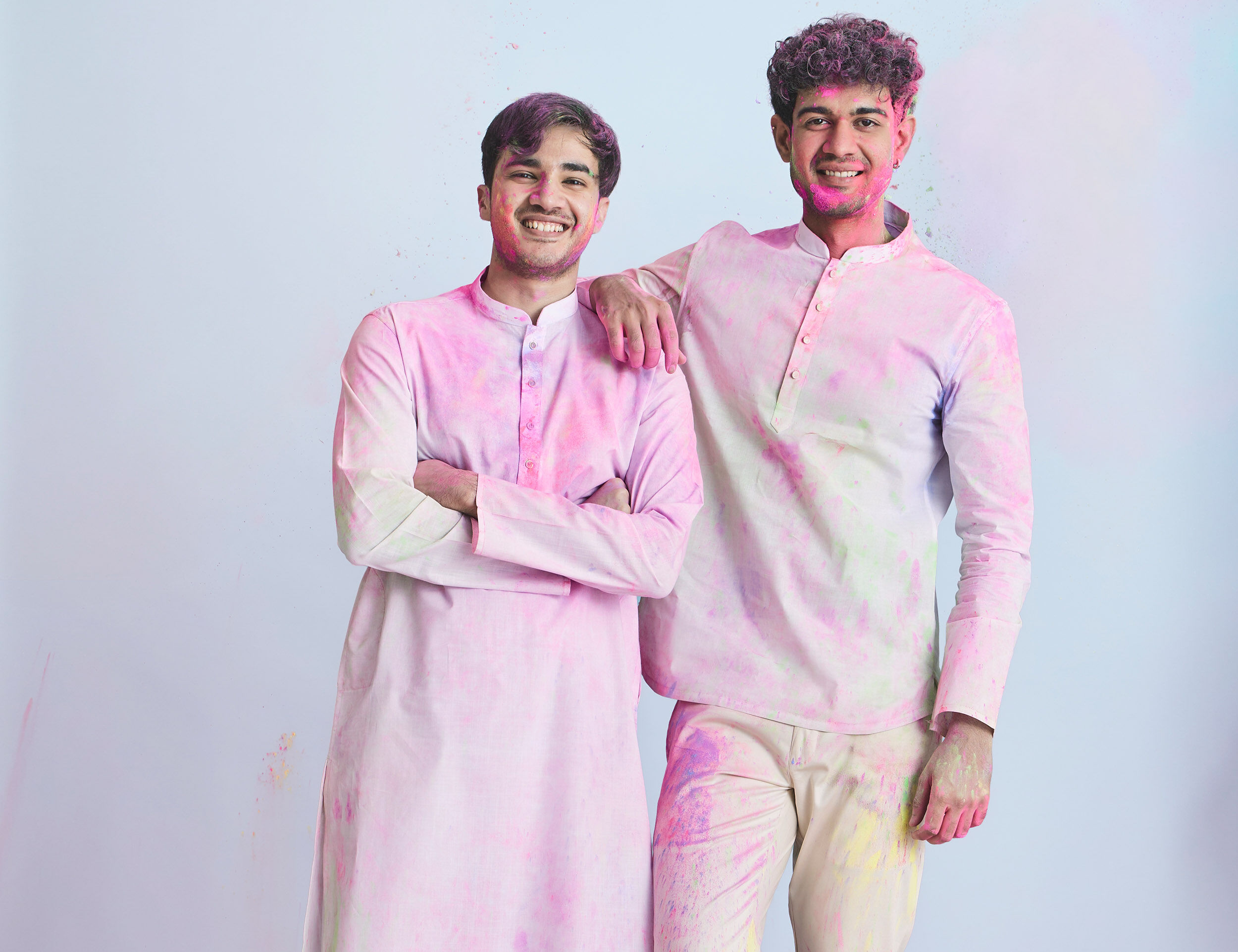 Men in pastel pink kurtas celebrating Holi, showcasing festive kurta styles with colorful powder.